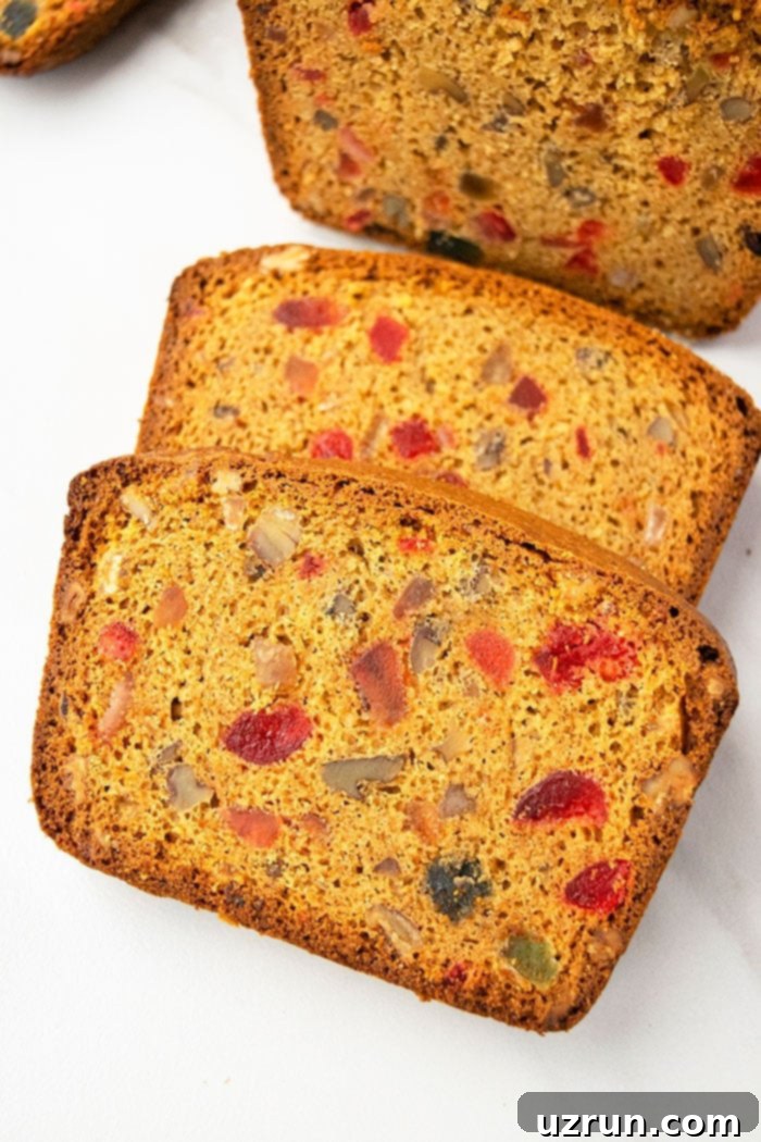 Effortless Christmas Fruit Cake Using Cake Mix 2 Slices of a perfectly baked, moist Christmas fruit loaf on a clean white background, showcasing the colorful candied fruits and nuts.