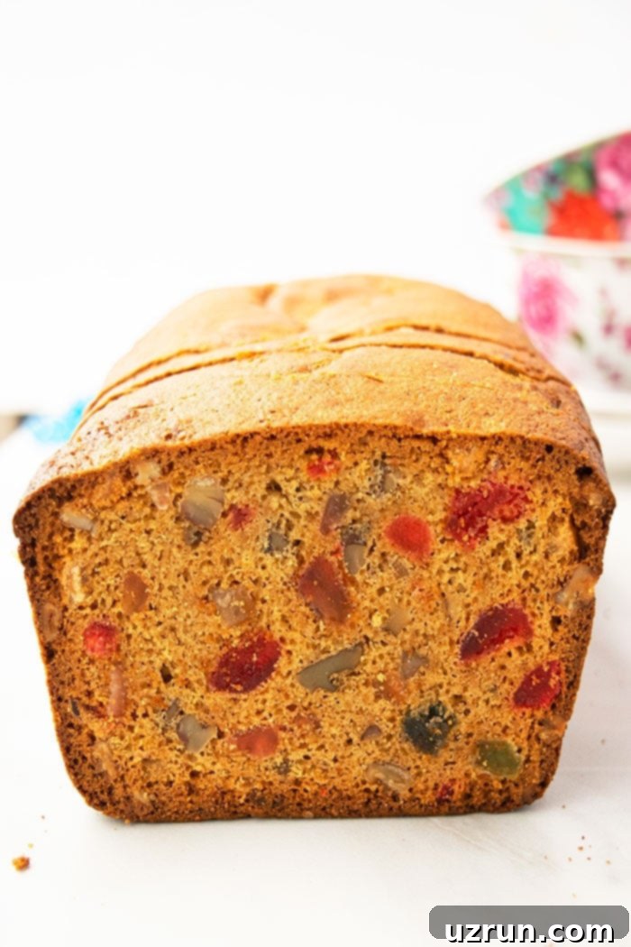 Effortless Christmas Fruit Cake Using Cake Mix 3 Closeup shot of a moist Christmas fruit cake made with cake mix on a white background, highlighting its colorful candied fruit and nutty texture.