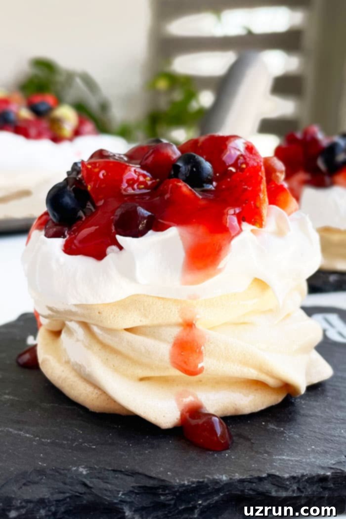 Easy Mini Pavlova Cake With Whipped Cream and Fresh Berries on Black Dish, showing a perfect, delicate meringue dessert topped with vibrant fruit.