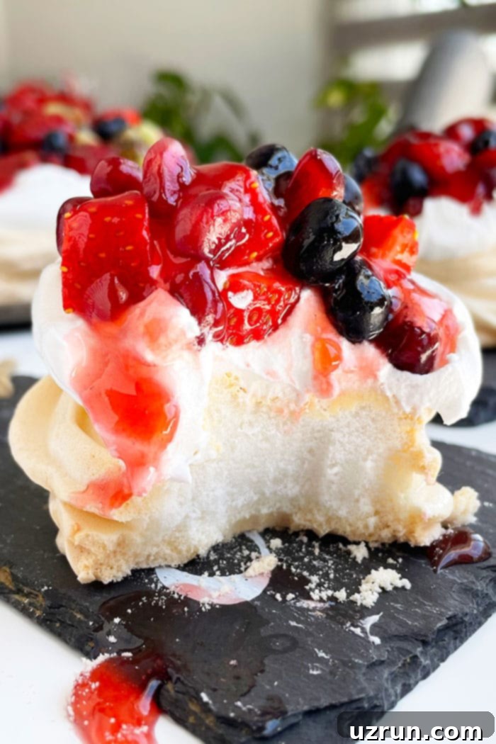Mini Pavlovas with Whipped Cream and Berries 4 Partially Eaten Pavlova Nests on Black Dish- Closeup Shot, showcasing the inviting texture and deliciousness of the dessert.