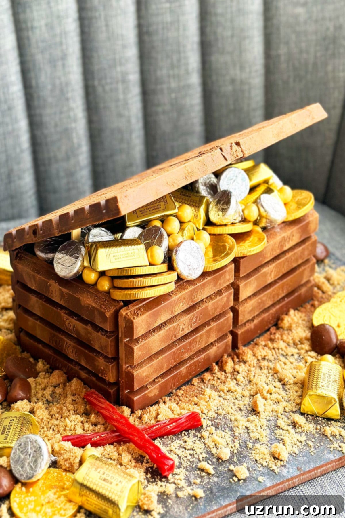 An inviting, beautifully decorated Easy Treasure Chest Cake with Kit Kat Chocolate, overflowing with gold and silver candies, set against a subtle gray background. Perfect for a pirate-themed birthday party.