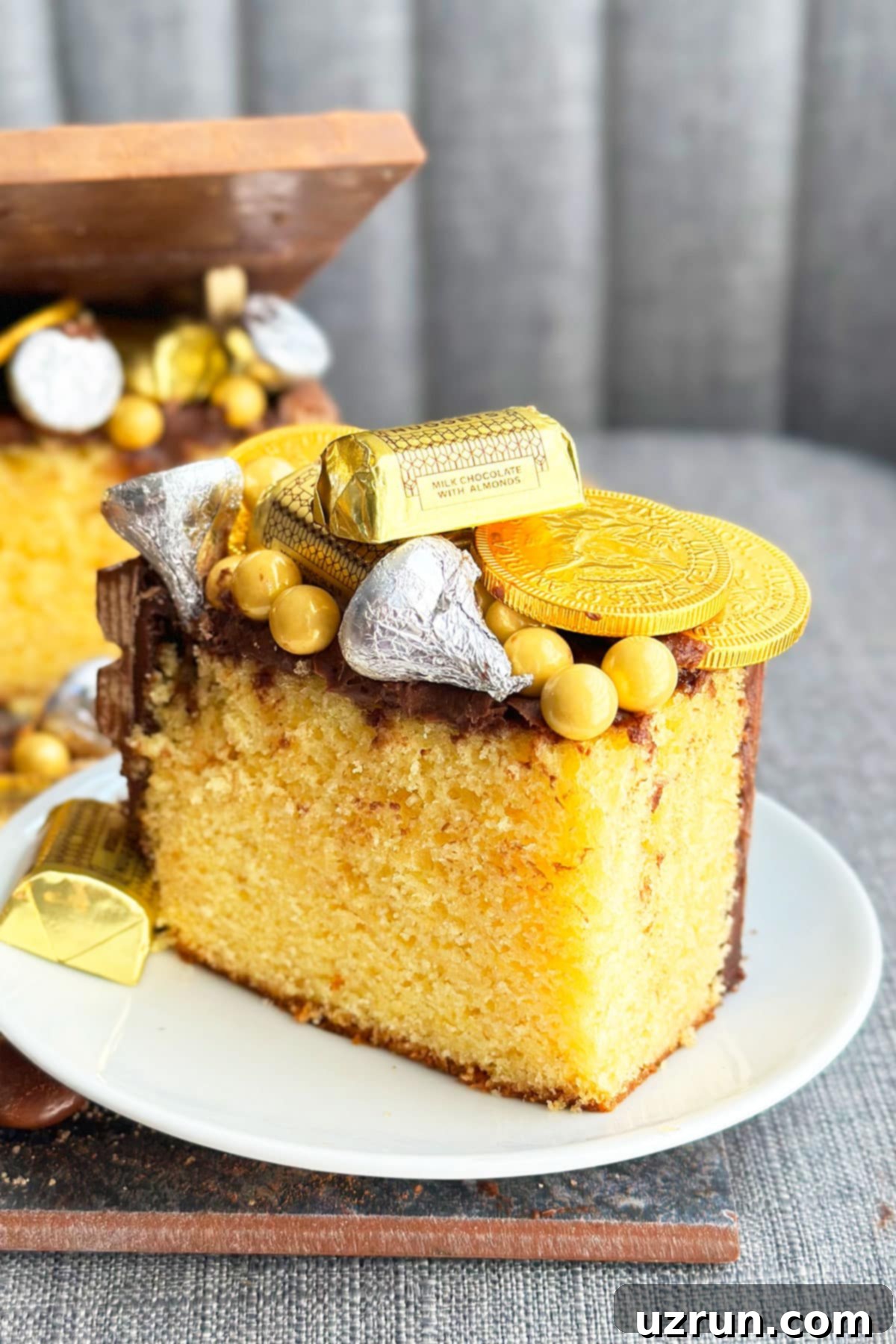 Kit Kat Treasure Chest Cake 6 A delicious slice of Vanilla Cake with rich Chocolate Frosting and vibrant candy decorations, beautifully presented on a pristine white plate, showcasing the edible treasure inside.