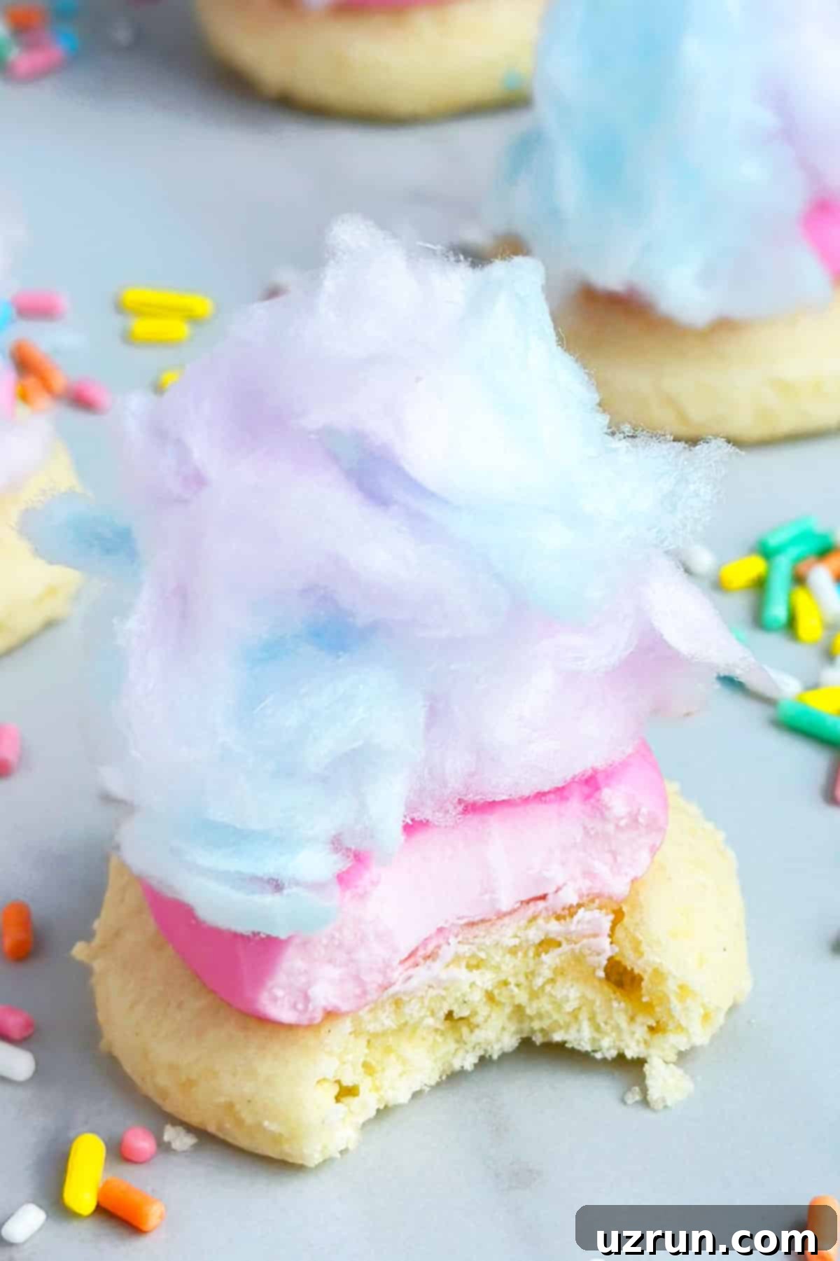 Easy Cotton Candy Cake Mix Cookies 4 Partially Eaten Sugar Cookie With Frosting and Candy on White Marble Background.