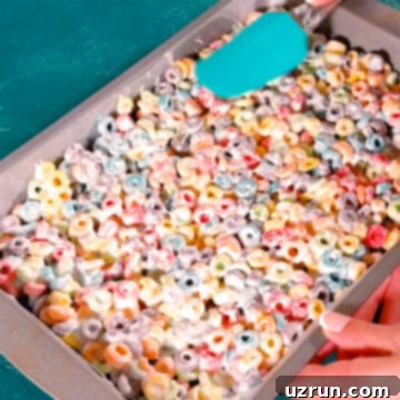 Three-Ingredient Rainbow Cereal Bars 11 Sticky mixture being spread evenly with a spatula in rectangle pan.