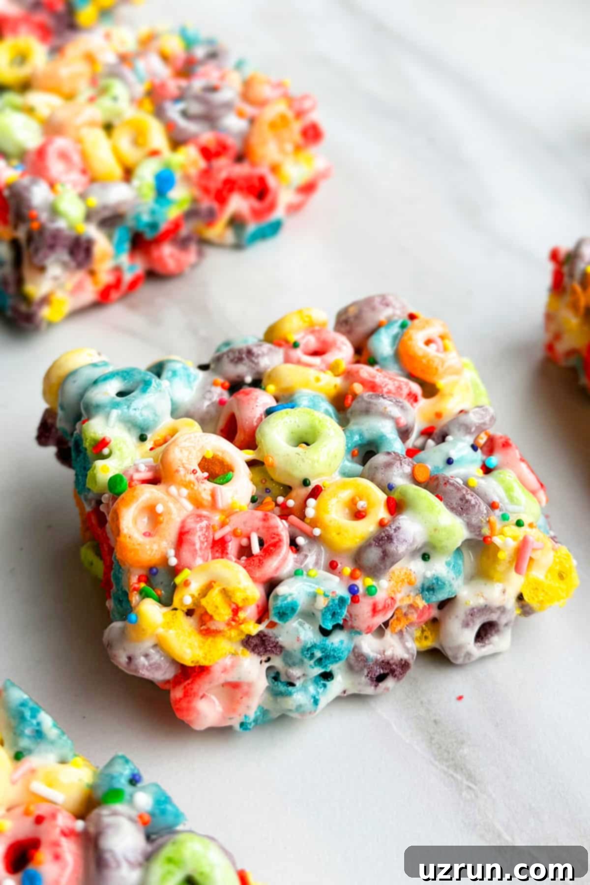 Three-Ingredient Rainbow Cereal Bars 3 Closeup Shot of Rainbow Bar on White Mable Background.