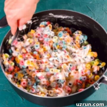 Three-Ingredient Rainbow Cereal Bars 9 Cereal being mixed with melted marshmallow mixture in nonstick pot.