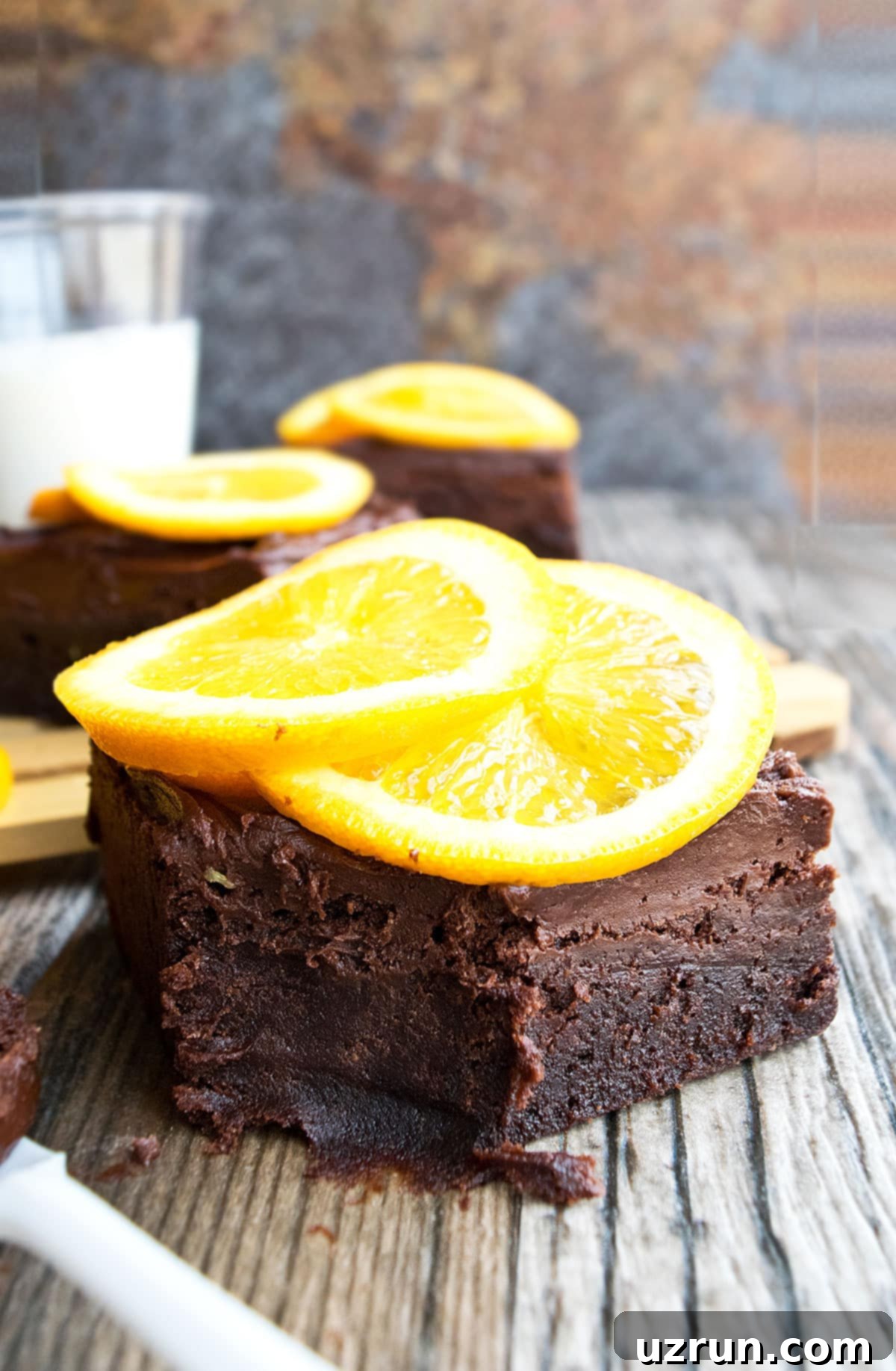 Fudgy Chocolate Orange Brownies 11 Partially Eaten Frosted Brownie on Rustic Brownish Gray Background.