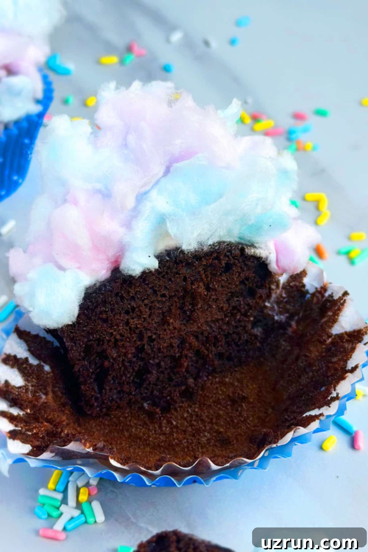 Easy Cotton Candy Cupcakes 3 Partially Eaten Cupcakes on Marble Background With Sprinkles.