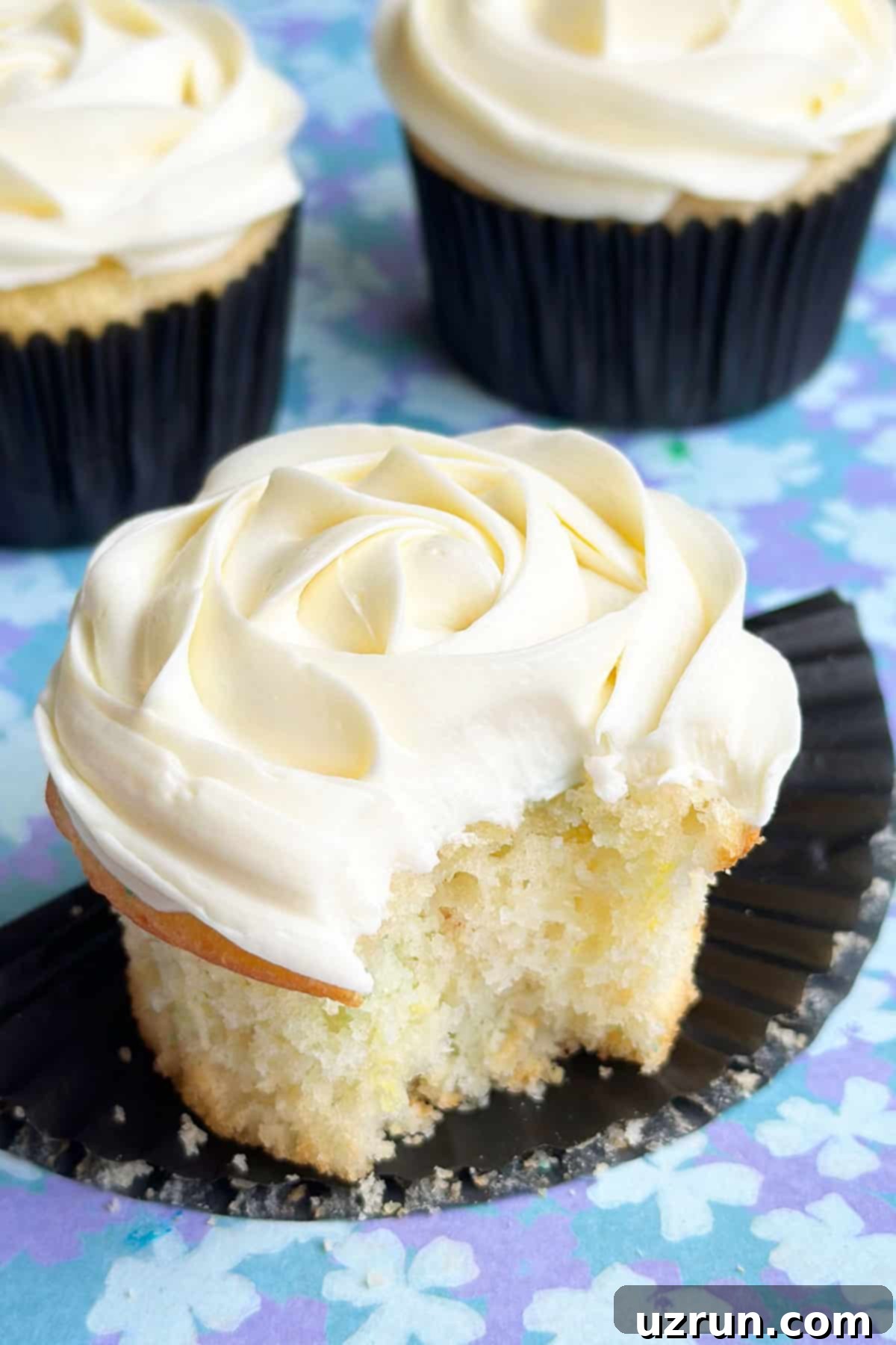 Moist Almond Sour Cream Cupcakes 5 Partially Eaten Cupcake With White Frosting on Black Liner.