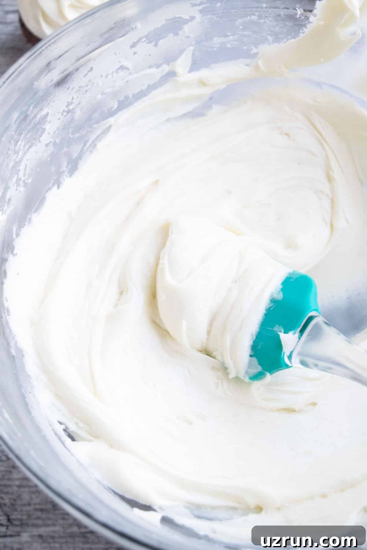 Easy Vanilla Sour Cream Frosting in Glass Bowl With Green Rubber Spatula. 