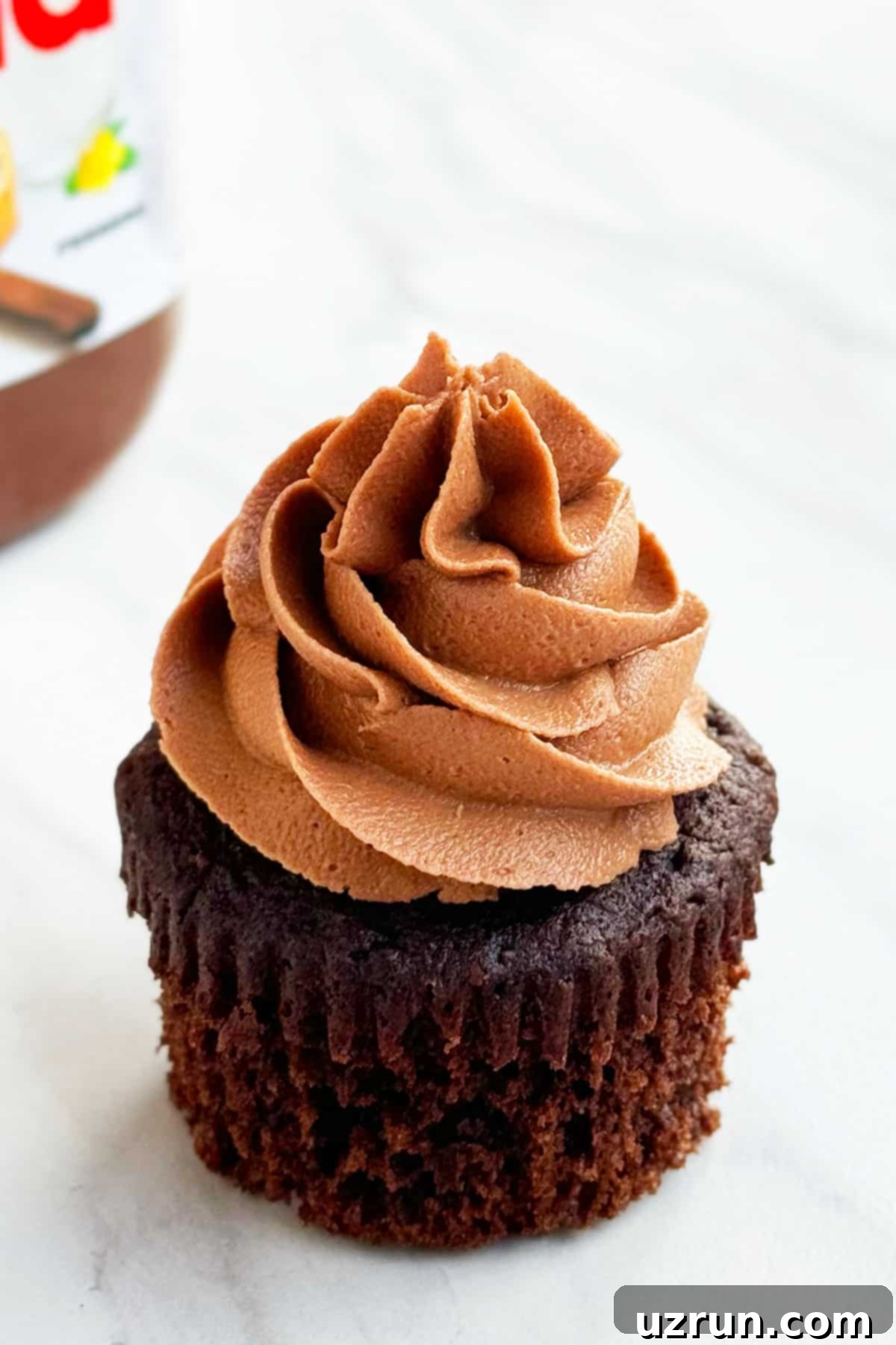 Effortless Nutella Cupcakes with Cake Mix 4 Frosted Chocolate Hazelnut Cupcakes With Liner Removed on White Marble Background.
