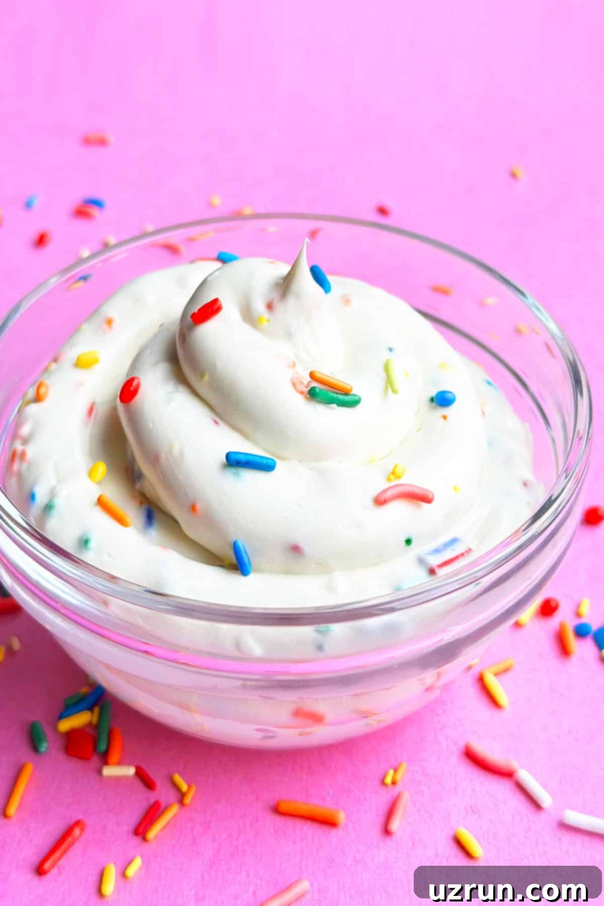 Glass Bowl of Cake Batter Dip Topped With Colorful Sprinkles on Pink Background. 