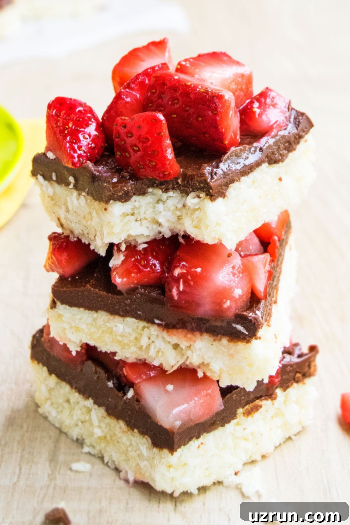 Chocolate Coconut Macaroon Bars 2 Stack of Easy Chocolate Coconut Bars on Wood Background, topped with fresh strawberries and chocolate drizzle.