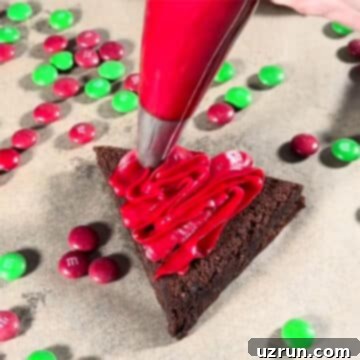 Christmas Santa Hat Brownie Bites 5 Piping red buttercream frosting in swirls on top of a triangle brownie, starting from the base.