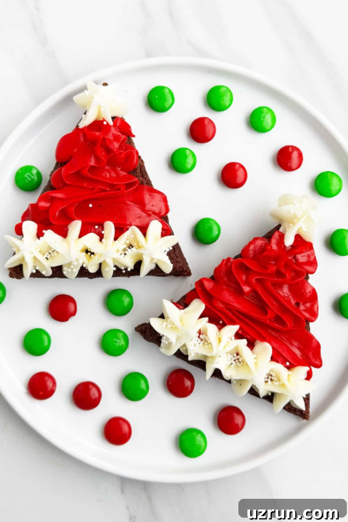 Christmas Santa Hat Brownie Bites 9 Easy Christmas Santa Claus Brownies Bites With Red and White Buttercream Frosting on White Dish With M&M Candies. A close-up of beautifully decorated Santa hat brownies with buttercream, alongside colorful M&M candies, ready for a festive celebration.