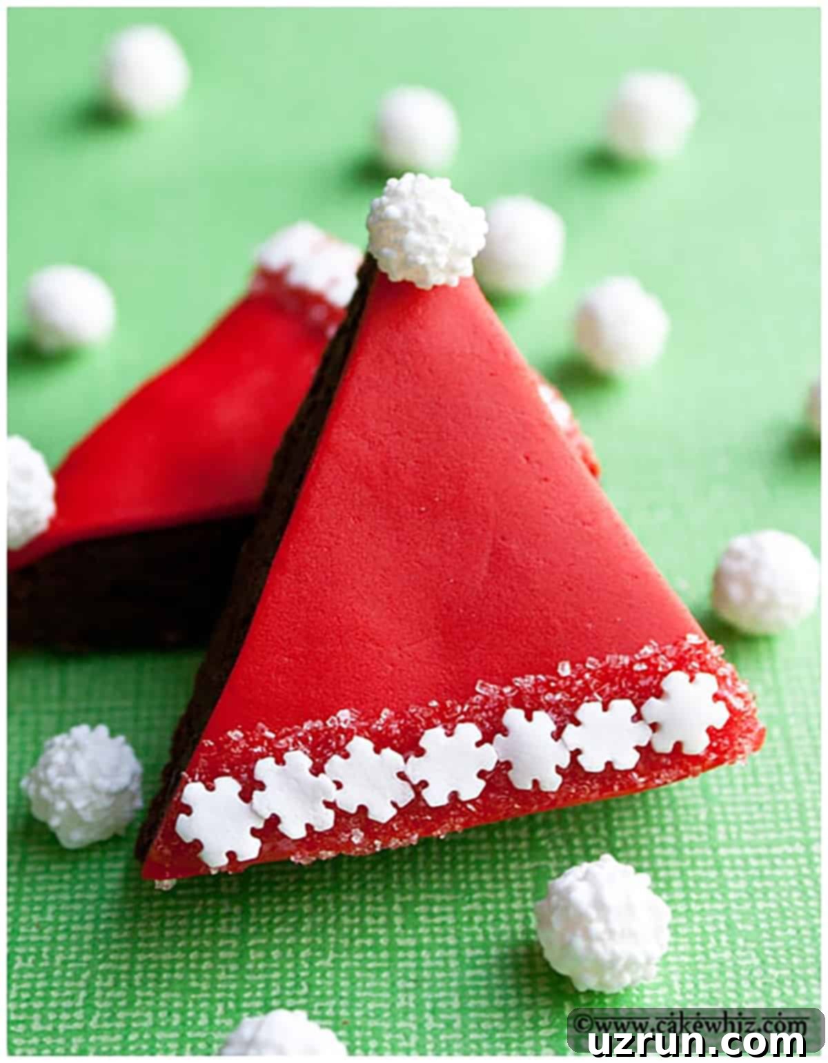 Christmas Santa Hat Brownie Bites 10 Easy Santa Brownies With Fondant on Green Background. Fondant-covered Santa hat brownies, showcasing a smooth red fondant, a white sparkling sugar brim, and a snowflake sprinkle pom-pom, on a festive green background.