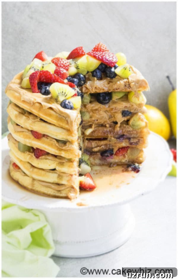 Waffle Cake Made Easy 3 Layer Cake With One Slice Removed on White Cake Stand, showing layers of waffles, peanut butter, and fruit.