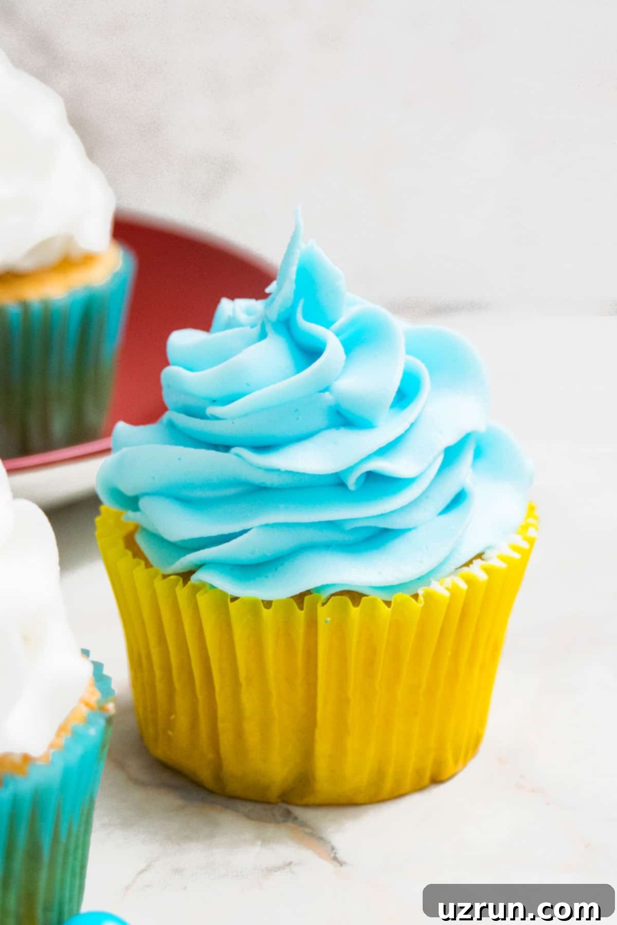 Easy Two-Ingredient White Chocolate Buttercream 8 Blue icing swirled on top of cupcake in yellow liner.