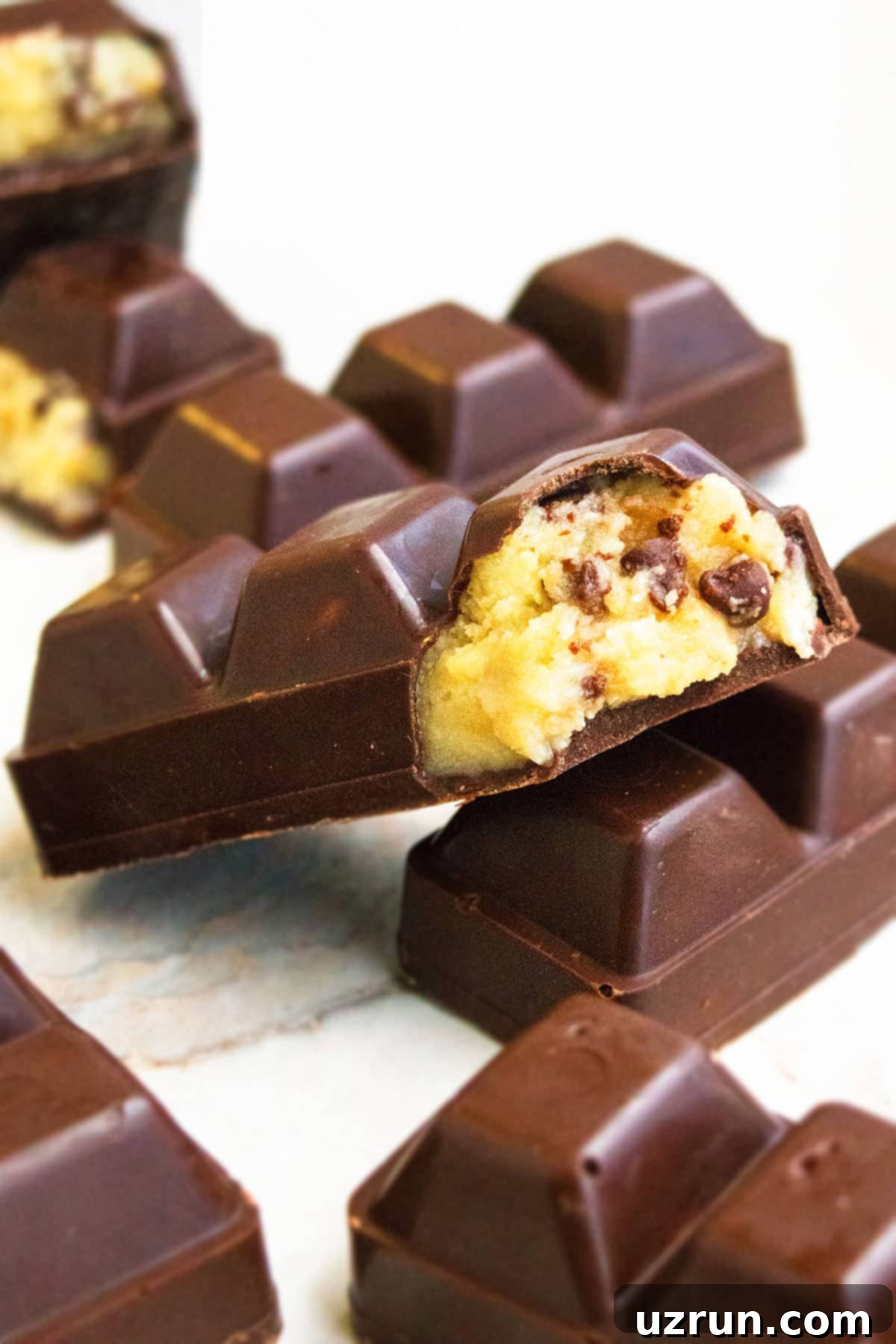 Eggless Chocolate Chip Cookie Dough Bars 3 Raw Healthy Chocolate Chip Bars on White Marble Background With Some Partially Eaten.