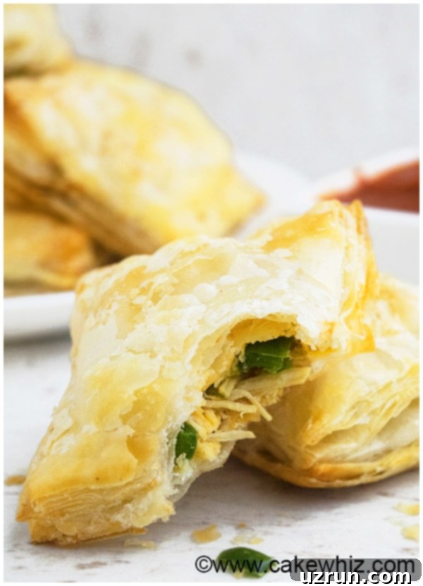 A stack of golden brown jalapeno chicken puffs on a plate, with one puff partially eaten, revealing the savory chicken and cheese filling.