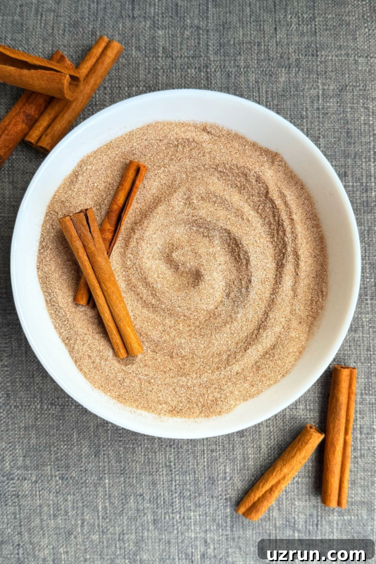 Effortless Homemade Cinnamon Sugar 2 Easy Homemade Cinnamon Sugar in White Bowl With Cinnamon Sticks on Gray Background.