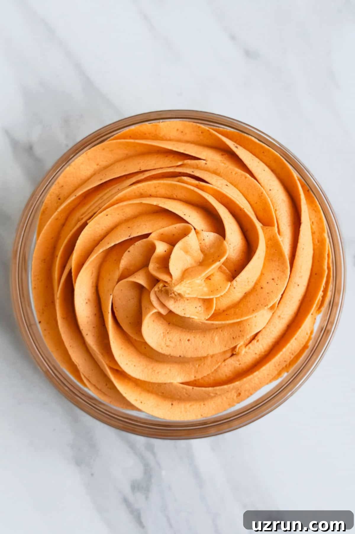Easy Pumpkin Cream Cheese Frosting 4 Glass bowl of spiced buttercream frosting on white marble background.