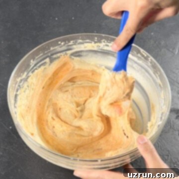 Easy Pumpkin Cream Cheese Frosting 9 Orange food coloring added to mixture and is being mixed with a blue spatula.