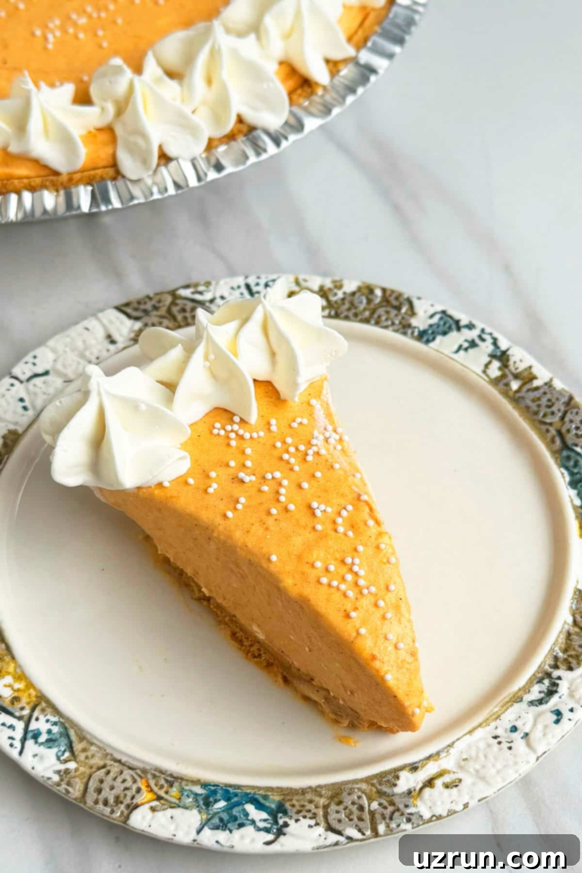 Velvet Pumpkin No-Bake Cheesecake 3 Slice of pie decorated with whipped cream and white sprinkles on a small dish.