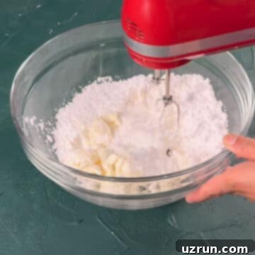 Velvet Pumpkin No-Bake Cheesecake 5 Powdered sugar and cream cheese being mixed in a glass bowl.