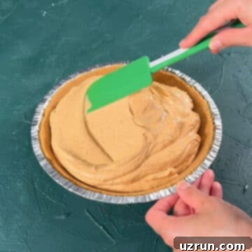 Velvet Pumpkin No-Bake Cheesecake 10 Green spatula being used to spread pie filling smoothly in graham cracker pie crust.