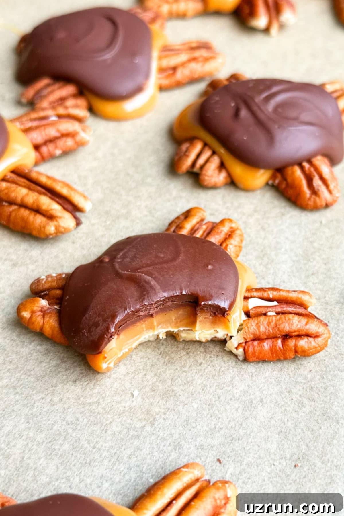 Decadent Homemade Chocolate Caramel Pecan Turtles 9 Partially eaten candy on brown wax paper.