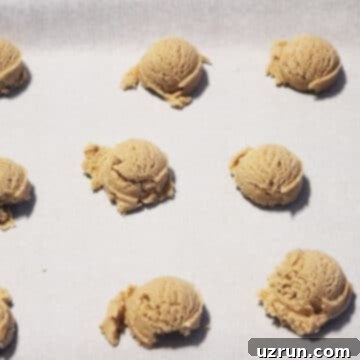 Effortless Soft Chewy Maple Cookies 7 Rough cookie dough balls dropped onto a baking tray with white parchment paper.