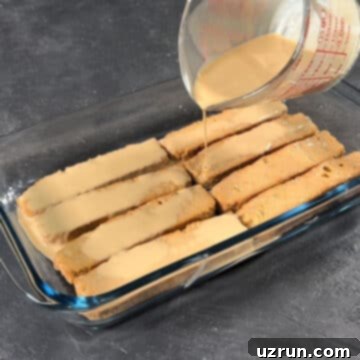 No-Bake Spiced Chai Tiramisu Cake 8 Chai soaked cake rusks arranged in a dish with more chai being poured on top.